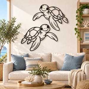 Puede incluir: Dos piezas de arte mural de metal negro con forma de tortugas marinas, cada una con un contorno suave y patrones de caparazón detallados. Las tortugas están colocadas en diagonal sobre una pared clara, mostrando un diseño tipo dibujo animado.
