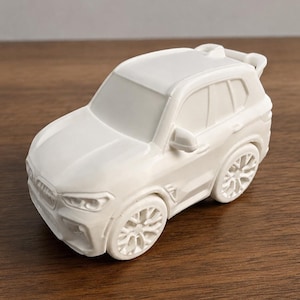 May include: A solid white, matte-finish toy SUV model featuring a detailed front grille, sculpted headlights, side mirrors, and multi-spoke wheels. The vehicle has a compact, stylized design with a rear spoiler and defined window outlines on the body.