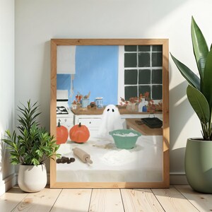 Peut inclure: Une impression d'art encadrée représentant une scène de cuisine avec un fantôme blanc, deux citrouilles orange, un rouleau à pâtisserie en bois et un bol vert rempli de farine sur un comptoir, devant un mur bleu et une fenêtre.