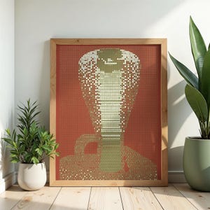 Può includere: Una stampa artistica da parete incorniciata raffigurante un cobra stilizzato composto da una griglia di piccoli punti. Il cobra è reso in tonalità verde chiaro e bianco su uno sfondo rosso intenso, il tutto racchiuso in una cornice in legno chiaro.