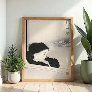 Può includere: Una stampa incorniciata che presenta un'illustrazione stilizzata di una persona con capelli scuri che appoggia la testa sulle braccia mentre guarda fuori da una finestra verso un paesaggio urbano piovoso. Include testo giapponese verticale.