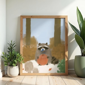 Peut inclure: Une impression d'art numérique encadrée représentant un raton laveur au nez bleu tenant un objet orange rond. Le raton laveur est situé dans une forêt avec des arbres et du feuillage bruns, sur un ciel bleu clair, le tout dans un cadre en bois clair.