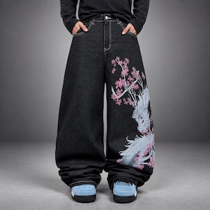 Könnte beinhalten: Weit geschnittene schwarze Jeans aus Denim mit einem großen hellblauen Drachenmotiv und rosa Kirschblütenzweigen auf dem linken Bein. Die Hose hat eine hohe Taille mit weißen Kontrastnähten, einen Knopfverschluss und Vordertaschen.