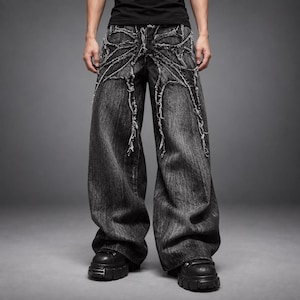 May include: Wide-leg denim jeans in a washed black finish featuring prominent distressed detailing. The front panels are adorned with frayed, web-like fabric overlays that extend from the waistband down to the mid-thigh area, creating a textured, layered appearance on the dark grey denim fabric.