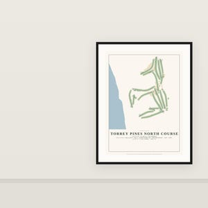 May include: A framed print featuring a map of the Torrey Pines North Course in La Jolla, California. The design displays green fairways against a cream background with a blue coastal edge. Text includes the course name, architect, and length.