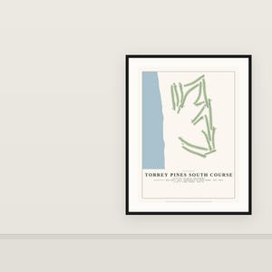May include: A framed print featuring a map of the Torrey Pines South Course. The design includes a light blue vertical strip representing the coast, green golf course fairways, and text reading TORREY PINES SOUTH COURSE, LOCATION: LA JOLLA, CALIFORNIA, ARCHITECT: WILLIAM F. BELL; REMODELED BY REES JONES | EST. 1957 | LENGTH: 7,802 YARDS | PAR 72.