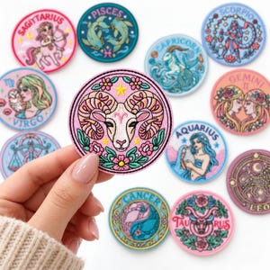 May include: A collection of circular embroidered patches featuring zodiac signs including Aries, Sagittarius, Pisces, Capricorn, Scorpio, Virgo, Gemini, Aquarius, Cancer, Taurus, and Leo, each with colorful illustrations and text labels.