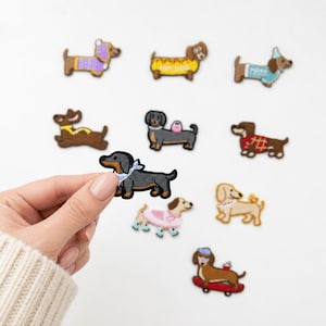 May include: A collection of embroidered dachshund patches featuring various designs, including dogs wearing sweaters, hats, and costumes, or riding a skateboard. One patch shows a black and tan dachshund wearing a light blue bandana.