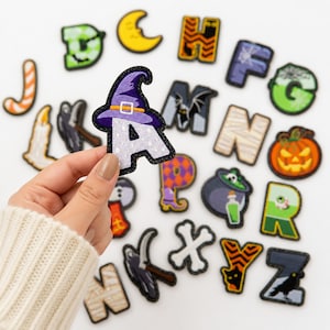 May include: A collection of embroidered alphabet patches featuring Halloween-themed designs such as a purple witch hat on the letter A, a pumpkin, a ghost, a bat, a mummy, a cauldron, and a black cat, with various letters displaying seasonal motifs.