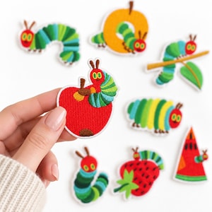 May include: A collection of embroidered fabric patches featuring the Very Hungry Caterpillar in various poses, including crawling on a red apple, a strawberry, a watermelon slice, and a branch, with vibrant green, red, and yellow thread colors.