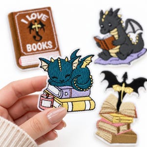 May include: Four embroidered patches featuring fantasy themes. One patch shows a brown book with the text I LOVE BOOKS. Another depicts a black dragon reading. A third shows a teal dragon sleeping on books with a candle. A fourth shows a black dragon on books.