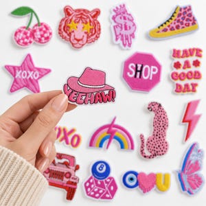 May include: A collection of embroidered iron-on patches featuring various designs including a pink cowboy hat with the text YEEHAW, cherries, a tiger face, a dollar sign, a leopard print sneaker, a star with XOXO, a stop sign with SHOP, and a rainbow.