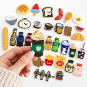 May include: A collection of small embroidered patches featuring various food and drink items, including a coffee cup with whipped cream, a burger, fries, soda bottles, bread, and snacks. The patches are colorful, detailed, and varied in shape.