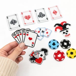 May include: A collection of embroidered patches featuring playing card suits, a royal flush hand, a jester hat, and circular poker chips in red, blue, yellow, and black. The patches are white with black and red thread details.