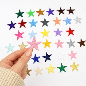 May include: A collection of small, five-pointed star-shaped embroidered patches in a wide variety of colors including red, blue, green, yellow, pink, purple, orange, brown, black, white, grey, and gold, arranged in a grid-like pattern.