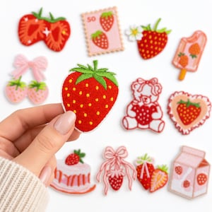 May include: A collection of embroidered patches featuring strawberry motifs, including a single strawberry held in the foreground, a postage stamp, a popsicle, a teddy bear, a heart, a cake, a milk carton, and various bows with strawberries.