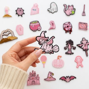 May include: A collection of embroidered iron-on patches featuring various pink and black Halloween-themed designs, including a witch on a broomstick, a ghost, a pumpkin, a skull, a bat, a castle, a spiderweb, a skeleton, and a cat.