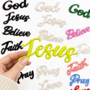 May include: A collection of embroidered fabric patches featuring the words God, Jesus, Believe, Faith, Pray, and Love in various colors including black, white, green, pink, blue, red, and a bright lime green patch held in the foreground.