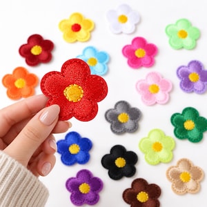 May include: A collection of small, five-petaled flower patches in various solid colors including red, yellow, white, green, blue, pink, purple, orange, gray, black, and brown, each featuring a contrasting yellow embroidered center detail.