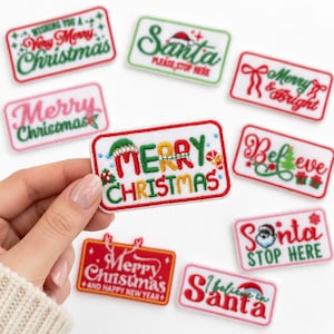 May include: A rectangular embroidered patch featuring the text Merry Christmas in red and green thread, accented with a small green Santa hat on the letter M and a candy cane, all outlined with a red border on a white fabric background.