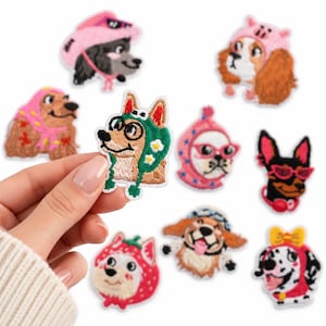 May include: A collection of embroidered fabric patches featuring various dog breeds wearing colorful hats and accessories. The designs include dogs in pink bonnets, strawberry hoods, green floral caps, and sunglasses, rendered in vibrant thread colors.