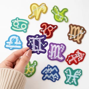 May include: A collection of twelve embroidered zodiac patches in various colors, each featuring a unique astrological symbol and its corresponding constellation pattern in white thread, including yellow, green, teal, red, brown, blue, and purple.