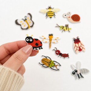 May include: A collection of embroidered insect and bug patches including a ladybug, bee, snail, butterfly, dragonfly, ant, beetle, and mosquito. The patches feature vibrant colors like red, yellow, brown, and black with cartoon-style designs.