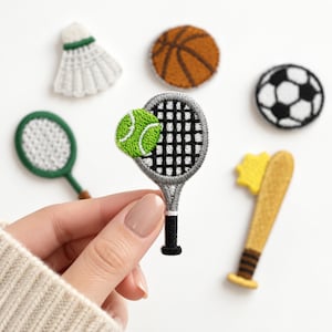 May include: A collection of embroidered sports patches including a white shuttlecock, an orange basketball, a black and white soccer ball, two green and white tennis rackets with a tennis ball, and a yellow baseball bat with a star detail.