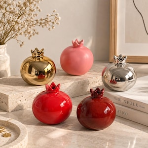 Peut inclure: Un ensemble de cinq vases en céramique en forme de grenade avec des finitions variées. Le lot comprend un vase doré métallique, un rose mat, un argenté métallique, un rouge vif brillant et un rouge bordeaux, chacun avec un sommet en couronne.