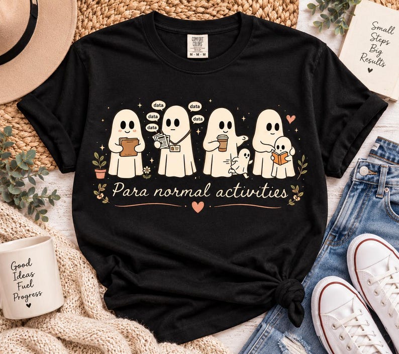 May include: A black short-sleeved t-shirt featuring a graphic of four ghosts engaged in various tasks with the text "Para normal activities" below them. The design includes small stars, hearts, and flowers in a light peach and white color palette.