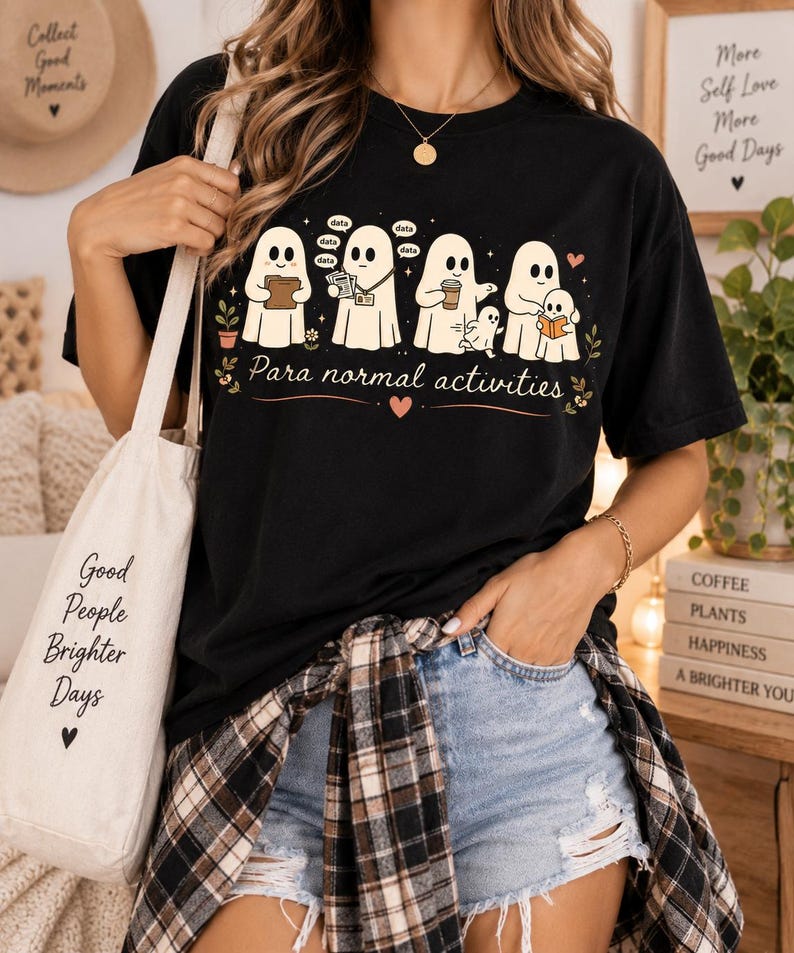 May include: A black t-shirt featuring a graphic of five white ghosts engaged in various tasks with the text "Para normal activities" printed below. The ghosts are shown holding a folder, papers, a coffee cup, and a book, with small speech bubbles.