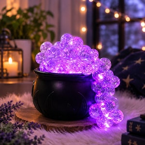 May include: A black cauldron filled with a cluster of glowing purple spherical lights. The lights are translucent with a textured surface, emitting a bright violet illumination that spills over the rim of the dark, rounded container.