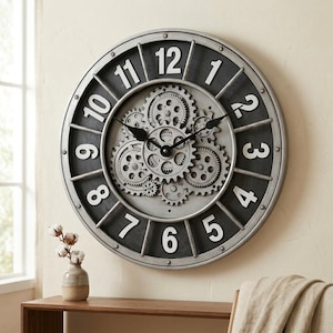May include: A round wall clock with a metallic silver frame and a dark grey face. The clock features large white numerals from 1 to 12 and a central mechanism of exposed, interlocking silver-toned gears with black hands.