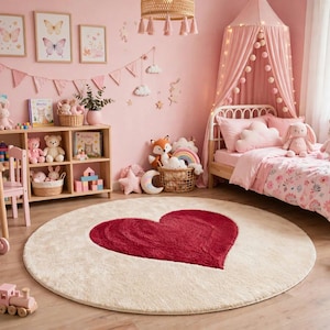 Può includere: Un tappeto rotondo con un grande cuore rosso scuro centrato su uno sfondo color crema. Il tappeto è posizionato in una camera da letto con pareti rosa, una struttura letto in legno con baldacchino rosa, una scaffalatura e vari peluche.