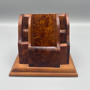 Puede incluir: Un organizador de escritorio de madera con un acabado marrón pulido y un patrón de veta de madera nudosa. La estructura incluye un compartimento central flanqueado por dos secciones laterales más pequeñas, sobre una base rectangular.