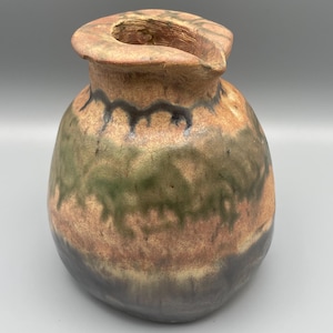Può includere: Una brocca in ceramica arrotondata con un bordo ampio e irregolare e un piccolo beccuccio. La superficie presenta una finitura terrosa e testurizzata con bande orizzontali di smalto nei toni del beige, verde muschio e grigio antracite.