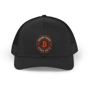 May include: A black trucker hat featuring a mesh back and a solid front panel. Centered on the front is an orange octagonal emblem with the text "GROUND POUND" and "STACK SATS" surrounding a prominent orange Bitcoin symbol in the center.