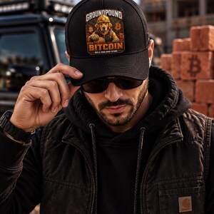 May include: A black baseball cap featuring a graphic print of a golden retriever wearing a construction hard hat. The text reads GROUNDPOUND BITCOIN BUILD YOUR OWN FUTURE. The design includes orange Bitcoin symbols on either side of the dog illustration.