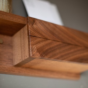 May include: A wooden wall-mounted key holder with a small drawer and a brass hook. The wood has a rich brown color and a natural grain pattern.