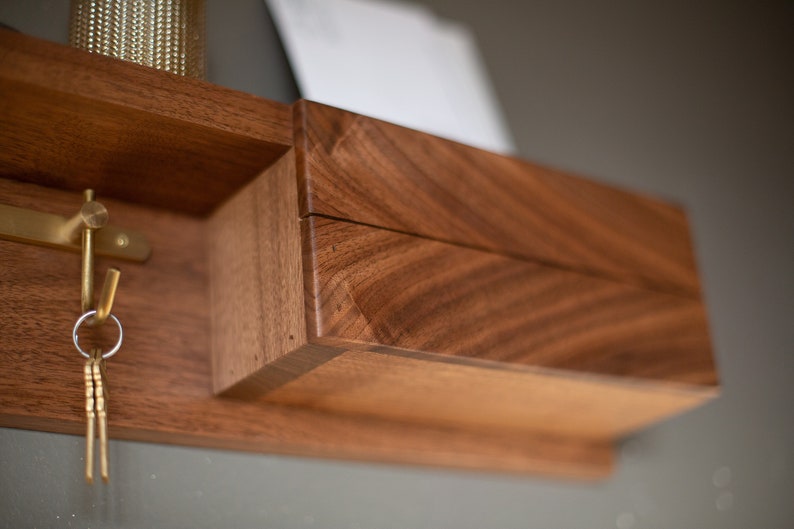 May include: A wooden wall-mounted key holder with a small drawer and a brass hook. The wood has a rich brown color and a natural grain pattern.