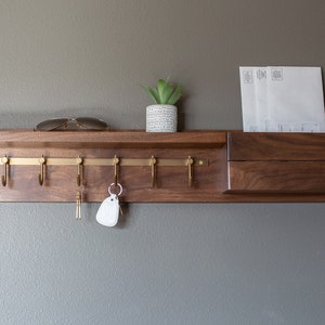 May include: A wooden wall-mounted key rack with a shelf and a mail slot. The rack has six brass hooks and a small potted plant on the shelf.