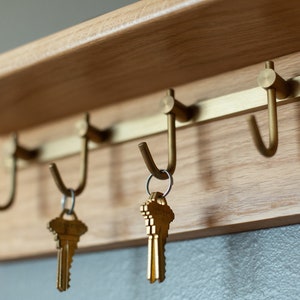 May include: A wooden key rack with three brass hooks and two sets of keys hanging from the hooks.