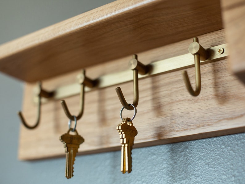 May include: A wooden key rack with three brass hooks and two sets of keys hanging from the hooks.