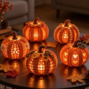 May include: Five orange crocheted pumpkins with internal warm lighting. Each pumpkin features unique textures, including openwork patterns, heart-shaped cutouts, small white floral accents, and pearl-like bead embellishments on the ribbed surfaces.