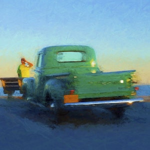 Op de afbeelding: Een vintage groene pick-up truck geparkeerd op een strand met een persoon die in de laadbak van de truck zit. De truck heeft een houten laadbak en een chromen bumper.
