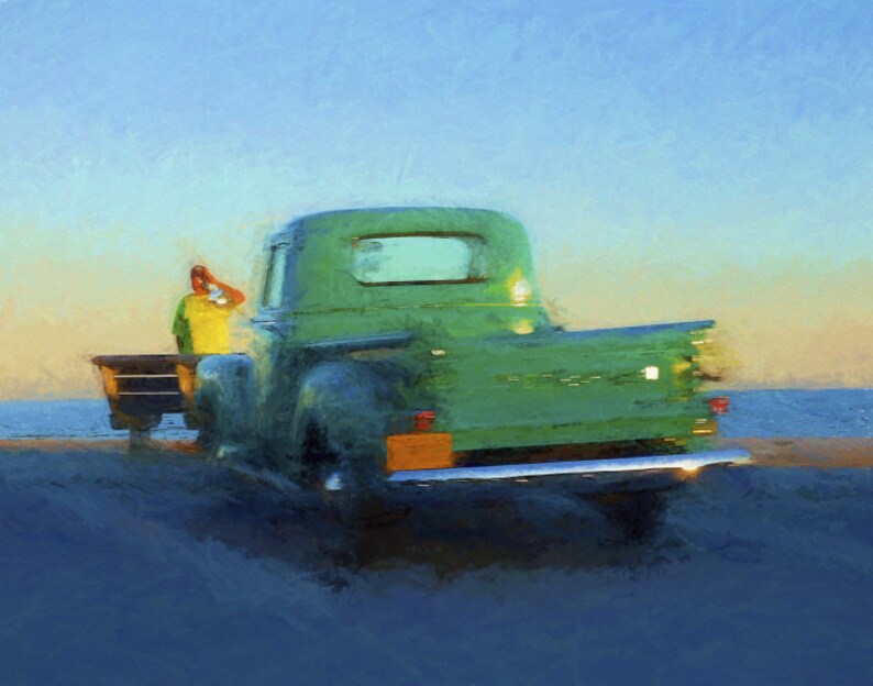 Op de afbeelding: Een vintage groene pick-up truck geparkeerd op een strand met een persoon die in de laadbak van de truck zit. De truck heeft een houten laadbak en een chromen bumper.