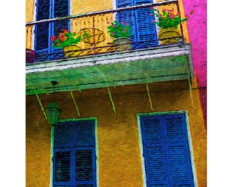May include: A yellow building with blue shutters and a balcony with potted plants. The building has a green awning and a white railing. The balcony has a wrought iron railing and a chair.