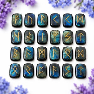 May include: A set of twenty-four rectangular labradorite stones arranged in a grid. Each polished stone features a dark blue and grey iridescent surface with a unique gold-colored engraved rune symbol on the front face of the smooth surface.