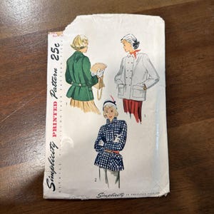以下が含まれることがあります： 3種類のジャケットスタイルが描かれたヴィンテージのSimplicity型紙封筒。デザインには、緑色のジャケット、明るい色のダブルブレストジャケット、青と白のチェック柄のジャケットが含まれています。封筒にはSimplicity 25cと記載されています。