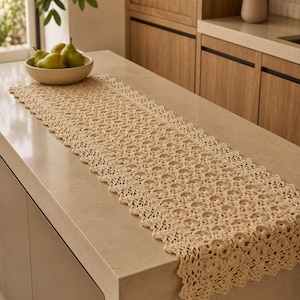 May include: A rectangular beige crochet table runner featuring a repeating circular pattern and a scalloped edge. The textile is crafted with intricate openwork stitching, creating a delicate lace-like texture that spans the length of the surface.